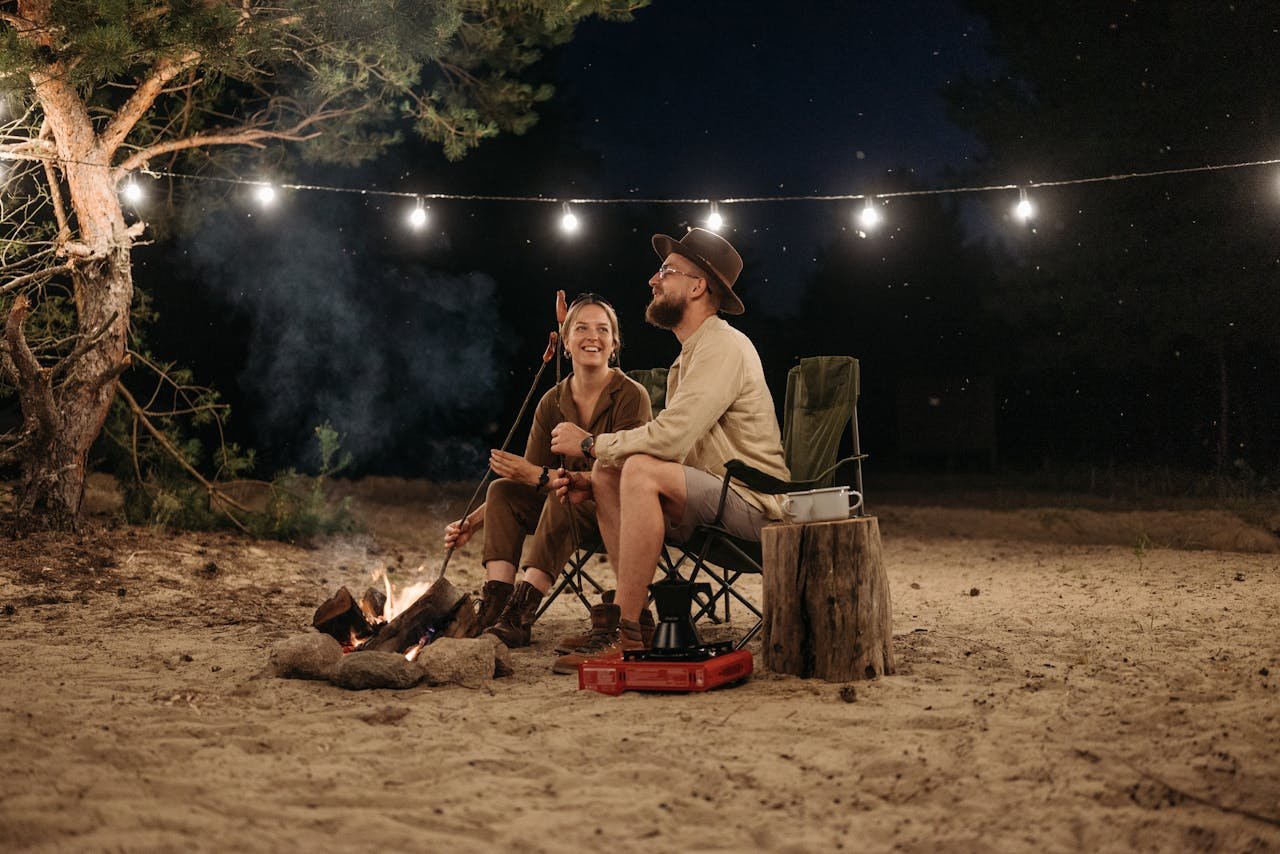 heros-img Happy couple sitting by a campfire, roasting sausages and enjoying the night outdoors.