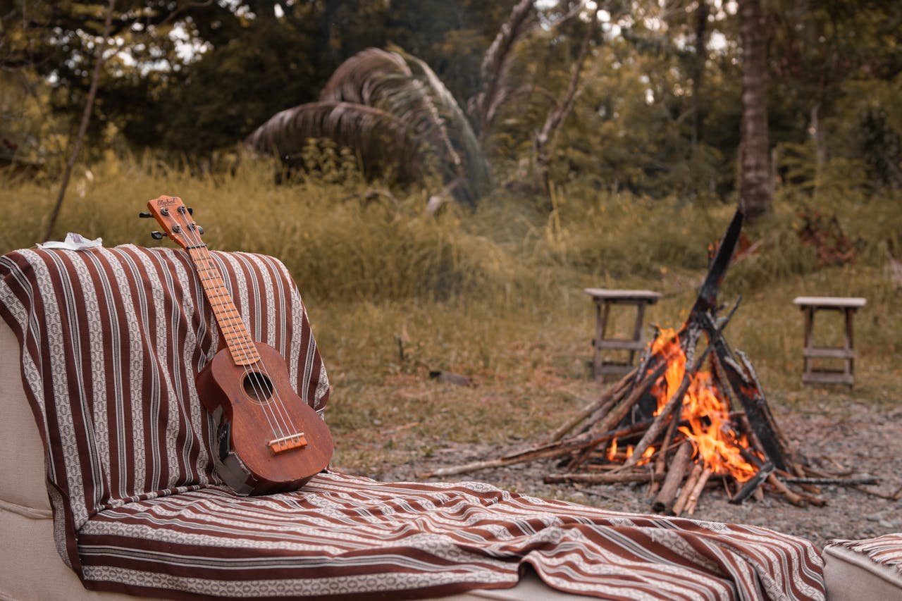 A serene campfire scene with a ukulele and patterned blanket outdoors.