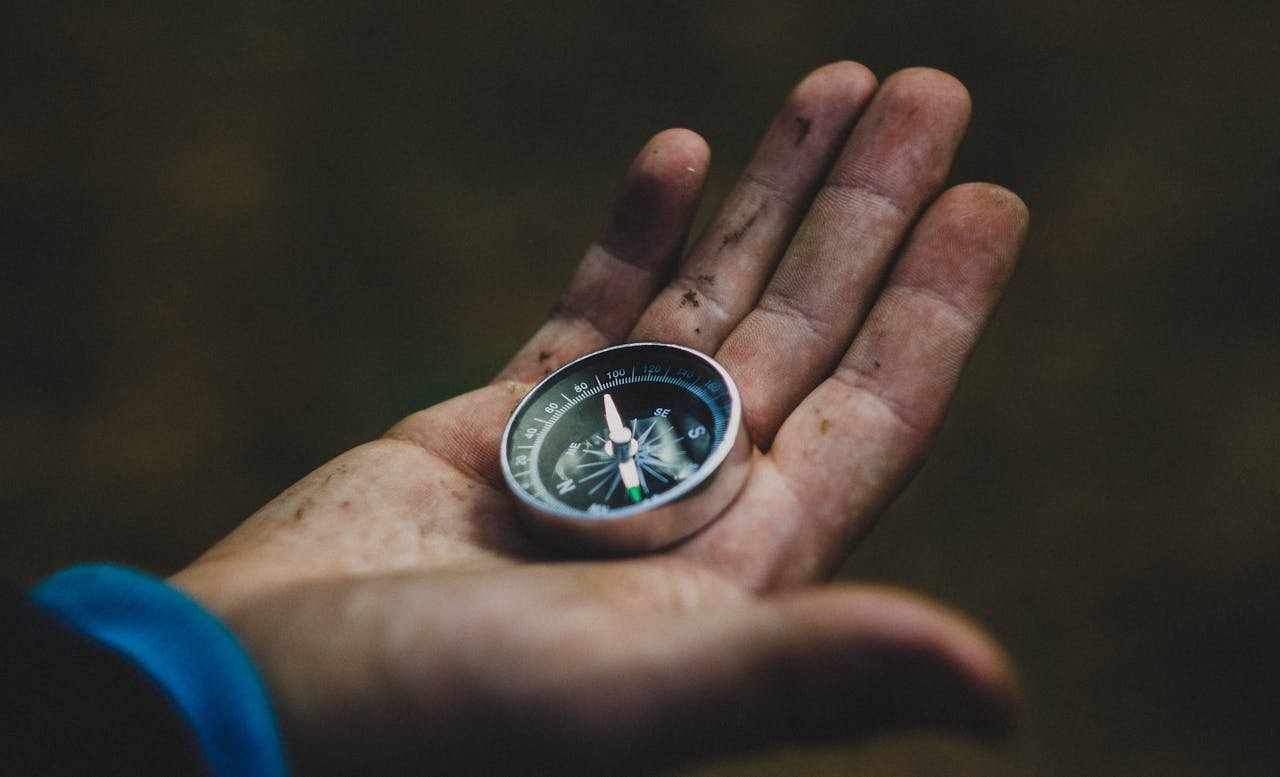 about-us-01 A close-up of a compass held in a dirty hand, symbolizing adventure and navigation.